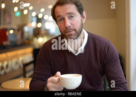 Casual wearing middle aged Caucasian male holding a white coffee mug in the coffee shop. Stock Photo