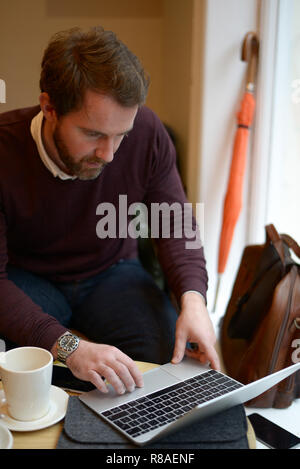 Casualty dressed young male using a laptop computer in the coffee shop with umbrella , coffee cup and mobile phone. Stock Photo