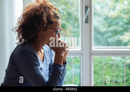 Portrait of pensive black woman standing beside window