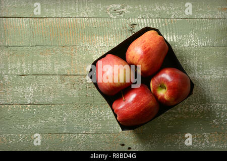 four red apples in the box on the green wooden table - closeup Stock Photo