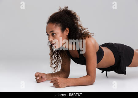 Portrait of an afro american young focused sportswoman doing plank exercise isolated over gray background Stock Photo
