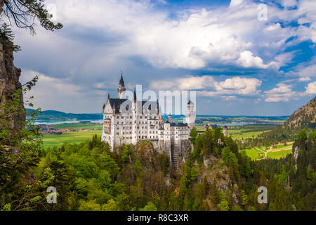 Panoramic view of the south façade of Neuschwanstein Castle surrounded by mountains. The popular tourist sight is a Romanesque Revival palace, built... Stock Photo