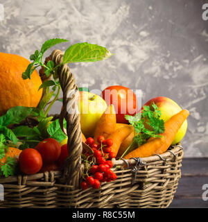 Autumn vegetables and fruits in wicker basket on grey background Stock Photo