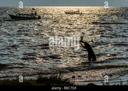 Passenger boats cruise past man casting fishing nets in late afternoon light on Lake Atitlan in Guatemalan highlands Stock Photo