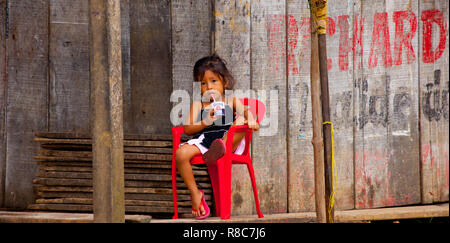 A litle girl having a juice in front of a wooden small shop in Iquitos Stock Photo