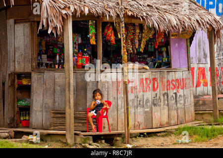 A litle girl having a juice in front of a wooden small shop in Iquitos Stock Photo