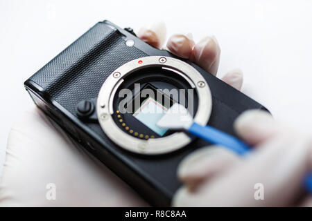 Close-up of mirrorless digital APS-C dirty camera matrix sensor cleaning and maintenance with swab, photographer cleaning photocamera on white backgro Stock Photo