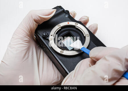 Close-up of mirrorless digital APS-C dirty camera matrix sensor cleaning and maintenance with swab, photographer cleaning photocamera on white backgro Stock Photo