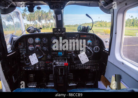 Air travel in Fiji, Melanesia, Oceania. View from a flight deck cockpit window of a small airplane to a lost remote airstrip overgrown with palms. Stock Photo