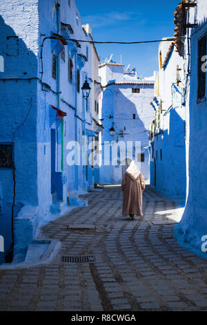 A man with a traditional dress is walking in the beautiful blue medina of Chefchaouen, Morocco. Stock Photo