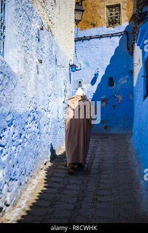 A man with a traditional dress is walking in the beautiful blue medina of Chefchaouen, Morocco. Stock Photo