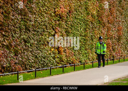 London, United Kingdom - November 12th, 2006: Unknown London Metropolitan police officer in high visibility jacket, walking in park, wall covered with