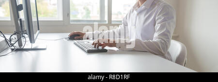 Wide view image of a student or programmer sitting at his desk working on office computer using keypad and mouse. Stock Photo