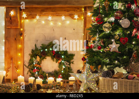 Beautiful Christmas setting, decorated fireplace with wooden mantelpiece fire surround, lit up Christmas tree with baubles ornaments, stars, lights, candles, vintage effect selective focus Stock Photo