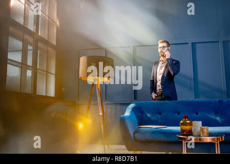 Portrait of an elegant businessman sitting with laptop on the couch at the luxury blue office interior Stock Photo