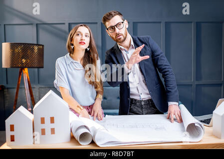 Young woman and man as an architects working with blueprints, laptop and house models in the office Stock Photo
