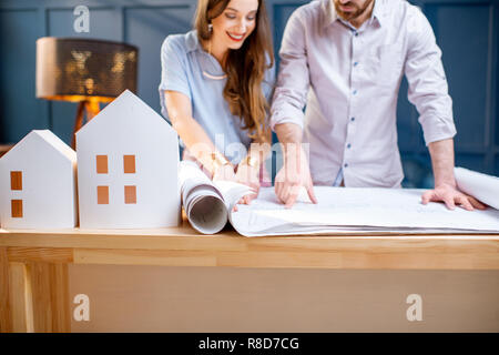 Young woman and man as an architects working with blueprints and house models in the office, close-up view Stock Photo