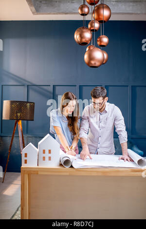 Young woman and man as an architects working with blueprints, laptop and house models in the office Stock Photo