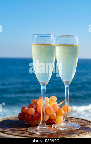 Champagne, prosecco or cava served with pink grape in two glasses on outside terrace with sea view close up Stock Photo