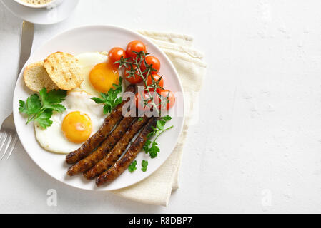 Fried eggs, sausages and cherry tomatoes on plate over white stone background with copy space. Dish for breakfast. Top view Stock Photo