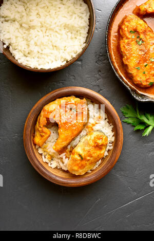 Delicious fish curry with rice in wooden bowl on black stone background. Indian style food. Top view, flat lay Stock Photo