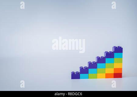 Colorful rainbow colored ascending stacks made of toy building bricks on gray background. Copy space. Stock Photo