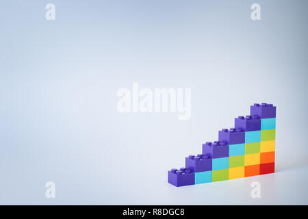 Colorful rainbow colored ascending stacks made of toy building bricks on gray background. Copy space. Stock Photo