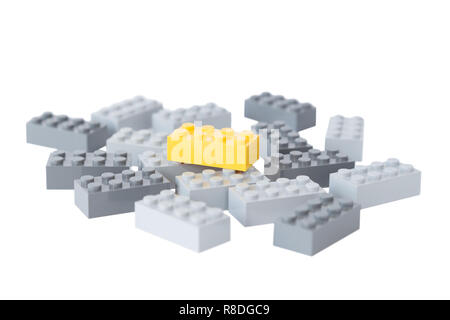 Pile of gray toy building bricks and one bright yellow on top of them. Concept photo of standing out from the crowd or gray masses. Isolated on white. Stock Photo