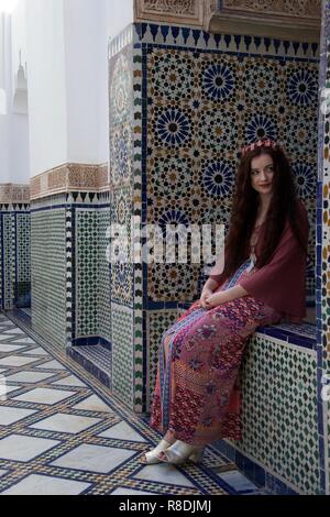 A hippie female causasian tourist with flowers in her hair sits in a Moroccan courtyard surrounded by elegant tiling Stock Photo