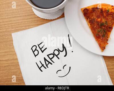 Photo image of motivational words be happy written on white paper on table with slice of pizza and a cup of coffee breakfast Stock Photo