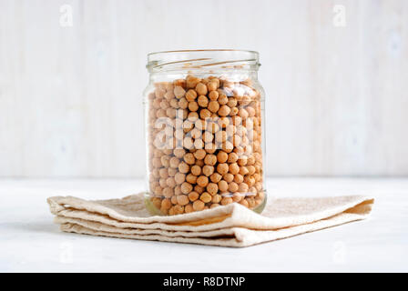 Large glass jar with healthy dried chickpeas on a folded cloth over a high key background in a side view with copy space Stock Photo