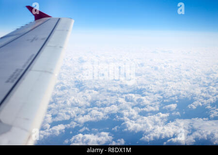 Looking to clouds through airplane window. And blured wing on the left. Stock Photo