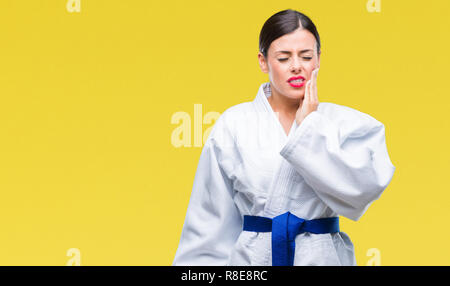 Young beautiful woman wearing karate kimono uniform over isolated background touching mouth with hand with painful expression because of toothache or  Stock Photo