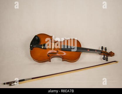 A brown violin with four strings and a violin bow on a white background Stock Photo