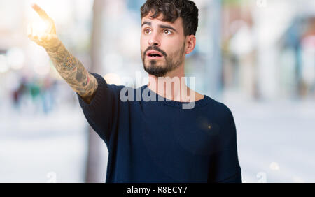 Young handsome man over isolated background Pointing with finger surprised ahead, open mouth amazed expression, something in front Stock Photo