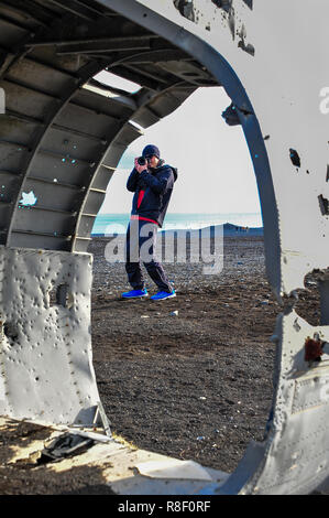 Man takes photograph into fuselage of crashed DC aircraft on Solheimasandur black sand beach near Vik. Stock Photo