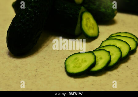 Green wet cucumbers with cut on yellow textured table Stock Photo