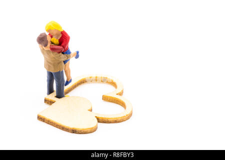 Miniature figures as in love hugging couple next to wooden hearts sign, isolated on white background Stock Photo