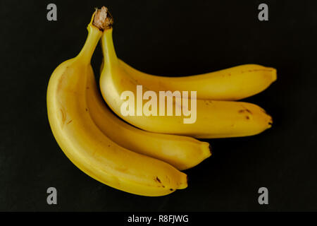 Bunch of yellow bananas on black background. Fresh and healthy. Shallow depth of field, focus on the front banana. Stock Photo