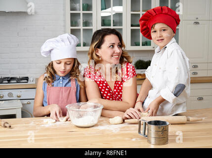 Happy mother with funny kids are preparing the dough, bake cookies in the kitchen Stock Photo