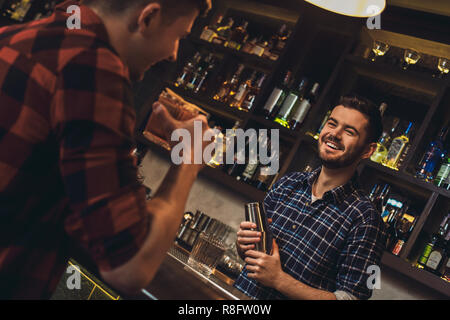 Young bartender standing at bar counter holding shaker talking with customer cheerful Stock Photo