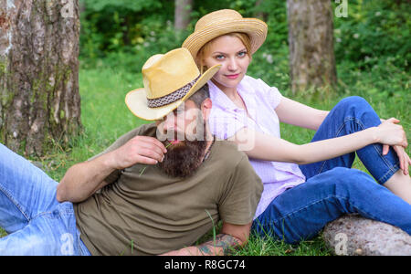 Couple in straw hats sit meadow relaxing. Reasons you should definitely wear more hats. Hats for tourism. Choose proper clothing and equipment to hike and forest picnic. Couple tourists wearing hats. Stock Photo