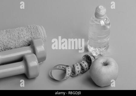 Athletics and weightloss concept. Dumbbells in bright green color, water bottle, measure tape, towel and fruit on green background. Barbells near juicy green apple. Sports and healthy regime equipment Stock Photo