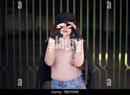 Street fashion outdoor photo of woman with dark hair in black leather jacket and sunglasses in defocus. Woman gesturing HEART with her hands - LOVE im Stock Photo