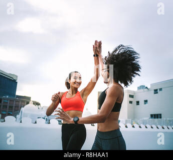 Two cheerful women in fitness wear giving high five while running on the terrace. Women athletes doing fitness training on the rooftop giving high fiv Stock Photo