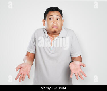 Photo image portrait of a cute young Asian man showing I don't know gesture, shoulder shrug and looking to the side Stock Photo