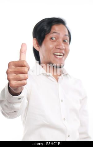 Photo image portrait of a cute funny young Asian man showing thumb up gesture with smiling face, close up portrait over white background, focus on han Stock Photo