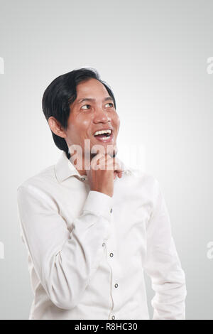 Photo image portrait of a funny young Asian businessman looking happy and smiling while thinking of something, close up portrait Stock Photo