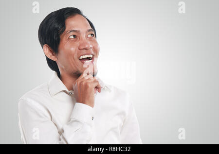 Photo image portrait of a funny young Asian businessman looking happy and smiling while thinking of something, close up portrait Stock Photo