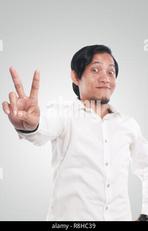 Photo image portrait of a cute funny young Asian man showing peace sign with smiling face, close up portrait over white background, focus on hand with Stock Photo